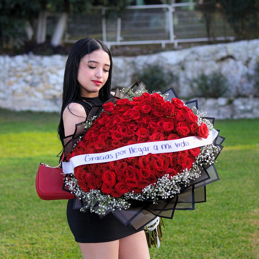 Mujer sosteniendo un gran ramo de rosas rojas con la dedicatoria “Gracias por llegar a mi vida” durante una experiencia romántica de Helicópteros VIP Monterrey.